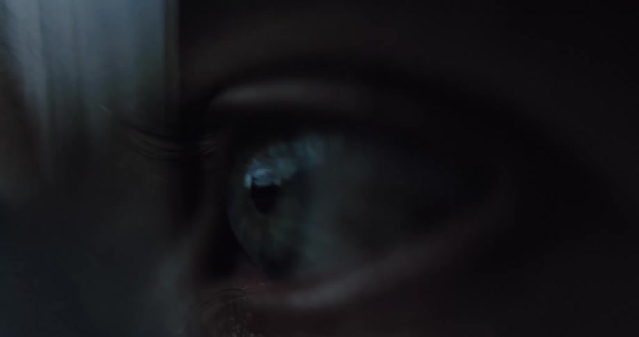 An extreme macro shot of a person's eye slowly opening in a dark, atmospheric setting