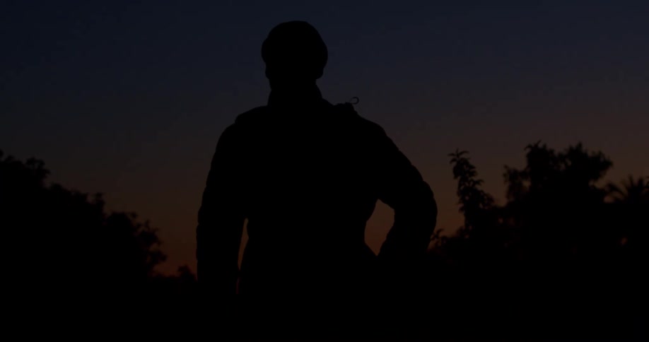 A silhouette of a person stands motionless against the dark sky during twilight