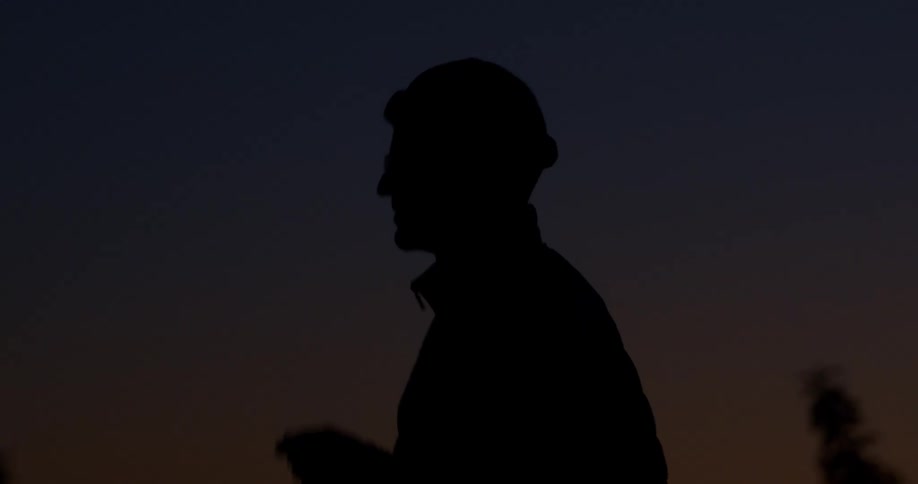 Silhouette of a man in a beanie exhaling in the cold against a twilight sky and then walking away