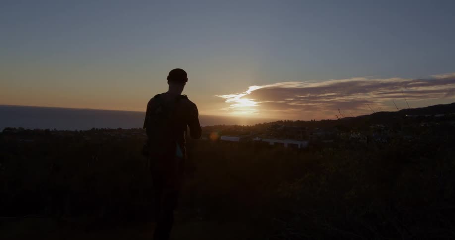 A man with a backpack walks to a scenic overlook to watch the sunset over the ocean and coastline