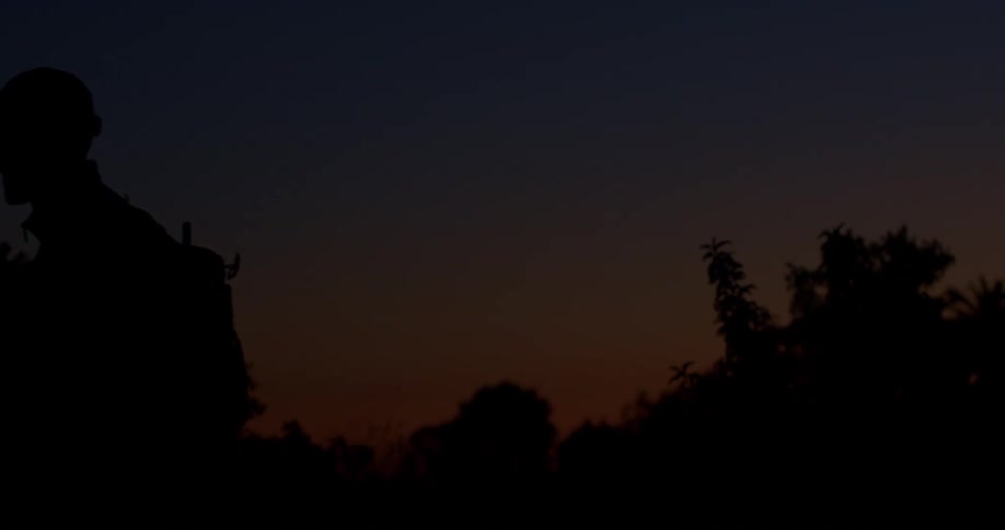 A lone silhouette of a person with a backpack walks out of the frame at dusk