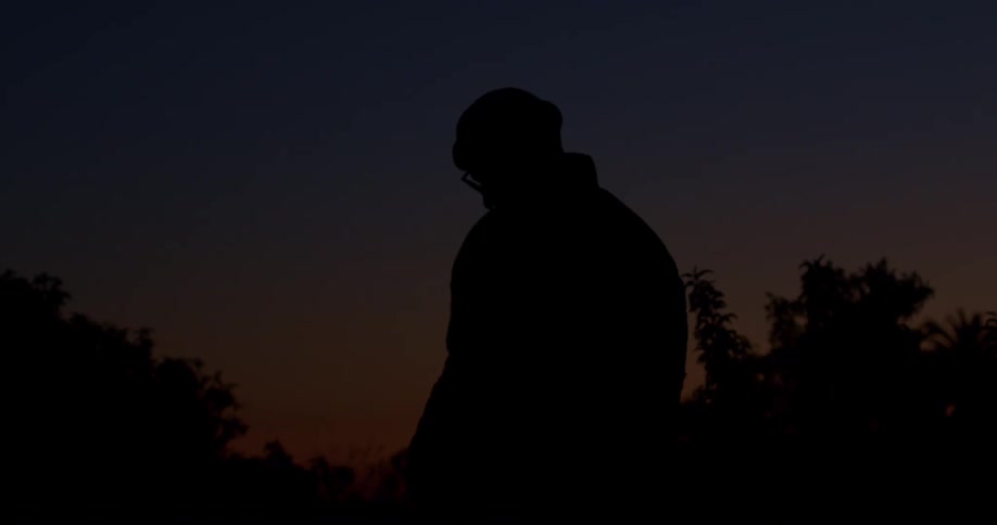 Slow motion silhouette of a pensive man in a jacket and beanie turning his head against the twilight sky