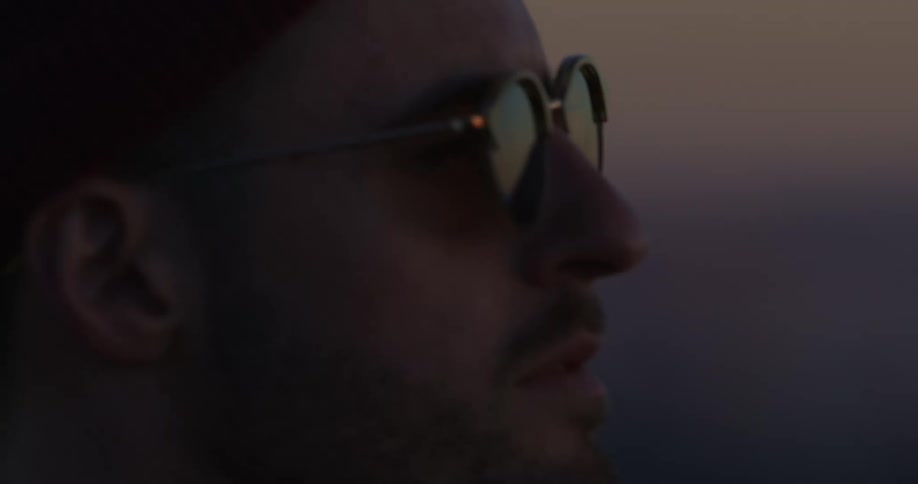 A rack focus shot transitions from a wide view of the Santa Monica coastline at sunset to a close-up of a man in sunglasses admiring the scene