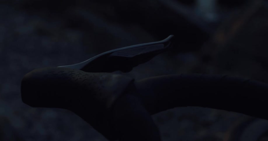A moody close-up shot of a bicycle's handlebars and brake levers in the dark, silhouetted by a soft, flickering campfire light