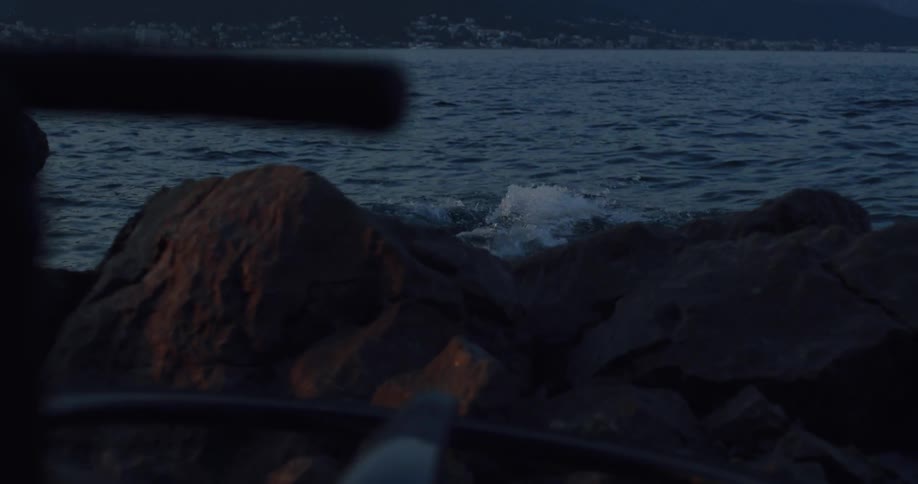 A man enters the dark water from a rocky shore at twilight and swims away