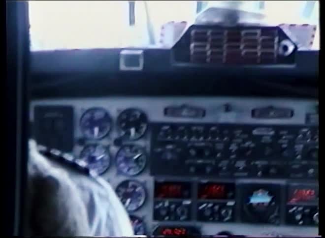 Archival footage from inside an airplane cockpit pans across the instrument panel and looks out onto a snowy runway in the mountains