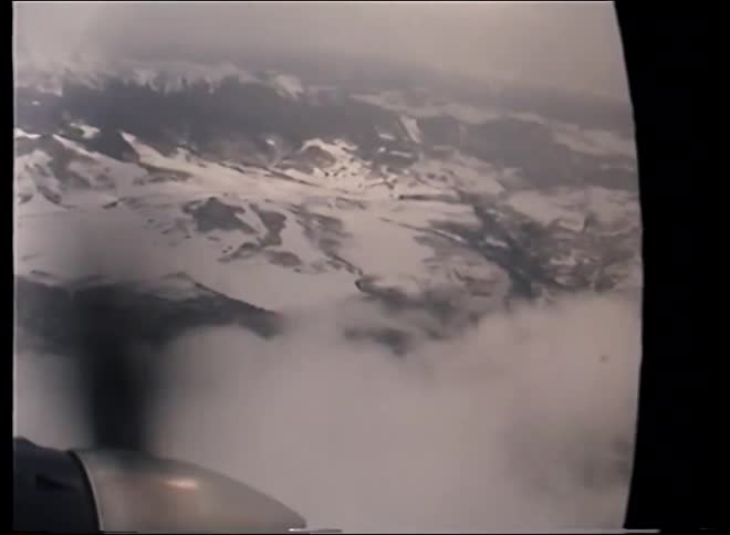 Vintage footage from a propeller plane window shows an aerial view of a vast, snow-covered mountain range