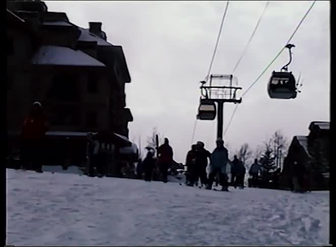 Silhouetted skiers stand on a snowy hill at a ski resort as a gondola lift passes overhead