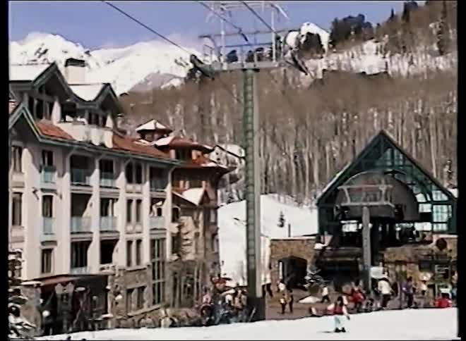 Retro home movie footage pans across a bustling ski resort village at the base of snow-covered mountains