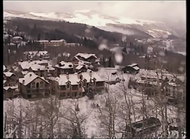 Vintage POV footage from a ski lift ascending over a snowy mountain resort village in the winter