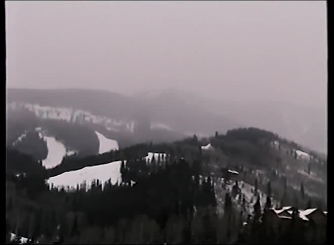 A slow pan reveals a vast, snowy mountain range with ski slopes and a resort on a foggy day