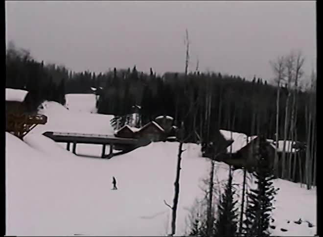 A vintage point-of-view shot from a moving chairlift at a ski resort reveals a lone skier on the slopes below