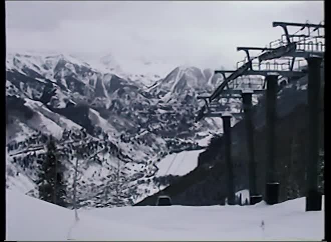 Vintage footage of a gondola ascending a snowy mountain at a ski resort with a vast mountain range in the background