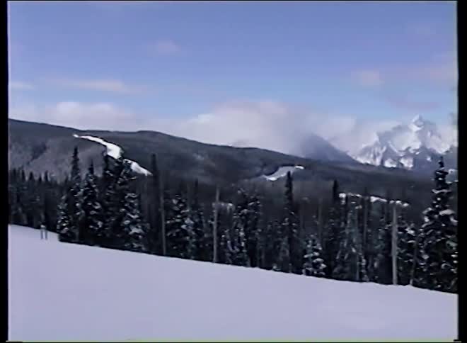 Vintage footage slowly pans across a majestic, snow-covered mountain range and evergreen forest