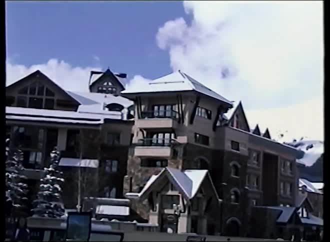 Vintage home movie footage captures children walking through a bustling ski resort village with stunning snow-capped mountains in the background
