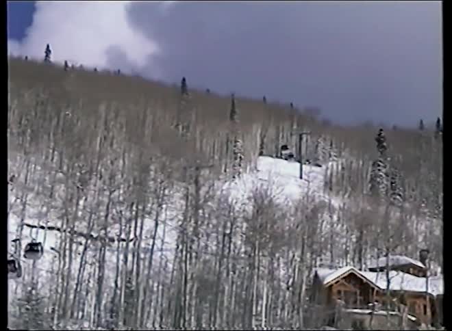 Nostalgic 1990s home movie footage of a bustling ski resort with gondolas, mountain chalets, and skiers below
