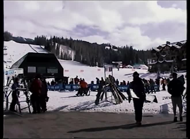 A slow pan reveals the bustling base of a mountain ski resort in this vintage-style footage