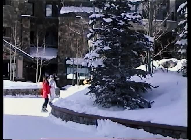 Vintage footage of a family playing in the snow outside a beautiful mountain ski resort on a sunny winter day