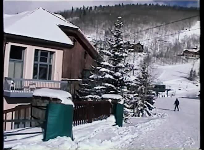 A vintage panning shot of a charming ski resort village with snow-covered buildings and slopes in the background