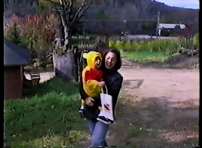 Vintage VHS footage shows a smiling mother holding her toddler dressed in a cute Winnie the Pooh costume for Halloween