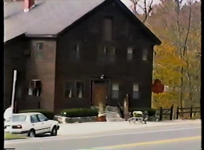 A slow zoom on the sign for 'The Old Mill' restaurant, a rustic building surrounded by colorful autumn foliage, captured on vintage video