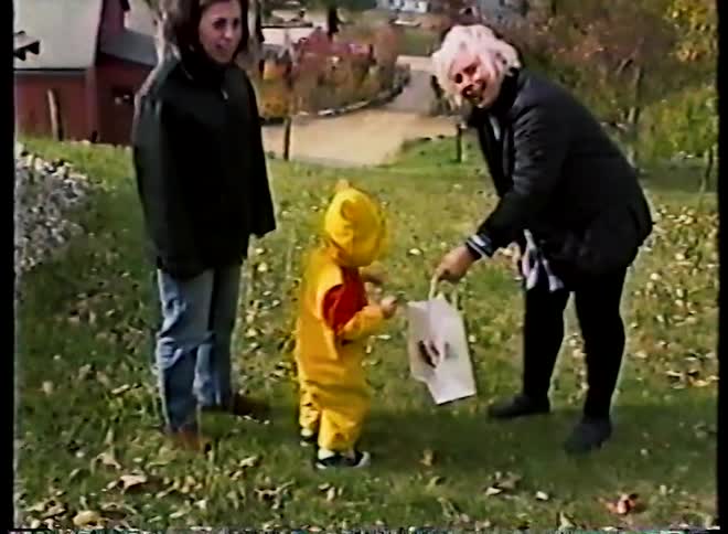 Vintage home movie footage shows a cute toddler in a Winnie the Pooh Halloween costume getting an apple from his grandmother in a grassy yard