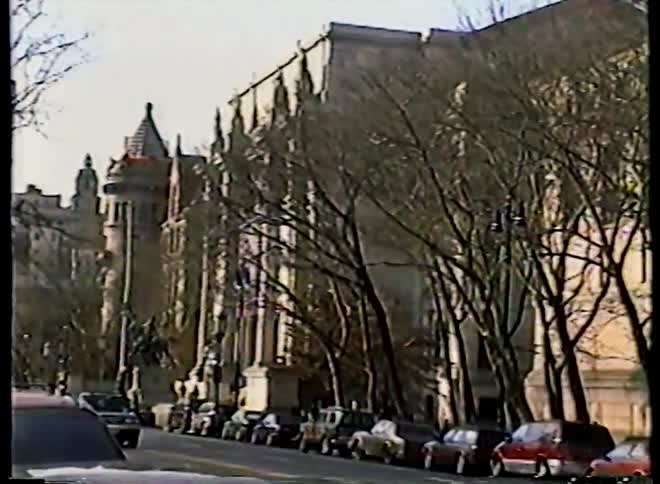 Vintage VHS footage captures a static shot of a grand, historic building along a New York City street lined with cars and bare trees