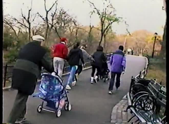 A slow-motion scene of families strolling with baby carriages along a winding park path during a cool autumn day