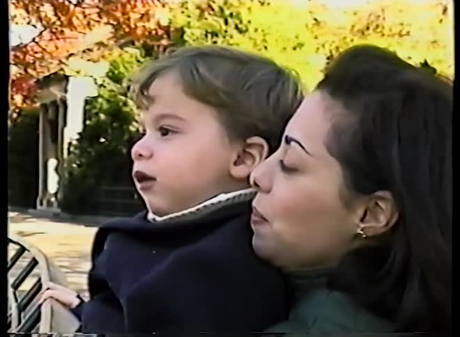 Vintage footage shows a loving mother holding her toddler son on a park bench as they watch something with wonder on a sunny autumn day