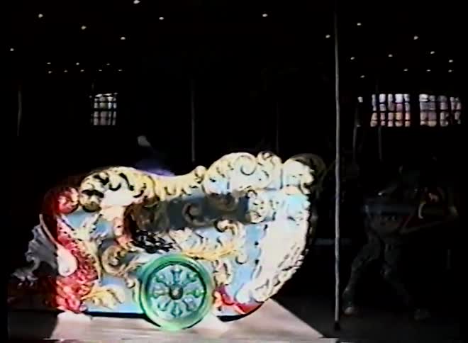 Vintage VHS footage shows an ornate carousel with people riding it as it slowly begins to turn, casting long shadows
