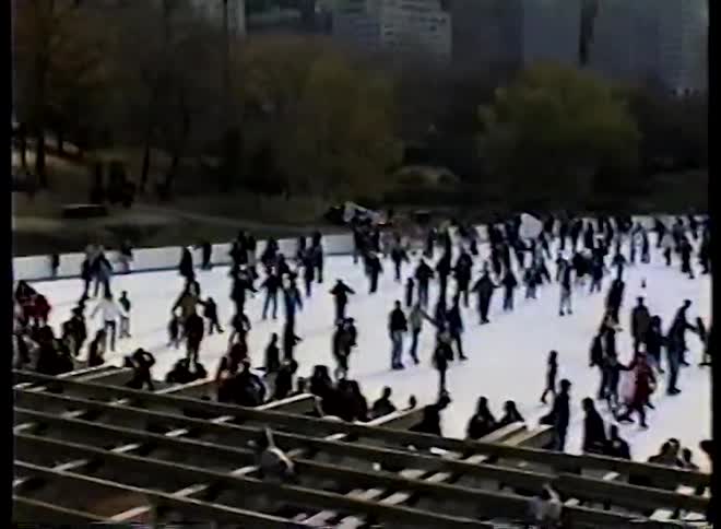 A high-angle vintage shot captures a crowded ice skating rink in Central Park before tilting up to the iconic New York City skyline