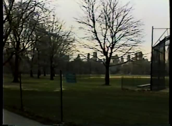 A vintage home video pans from an empty baseball field to people walking on a path in Central Park, New York City