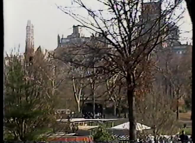 Vintage footage pans across a bustling autumn day in New York's Central Park, revealing crowds of people with city buildings in the background