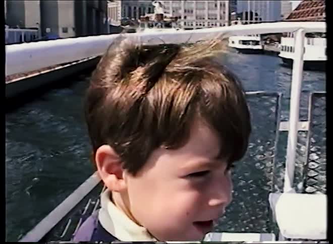 A cute little boy smiles for the camera before playfully eating a banana on a tour boat floating down a city river