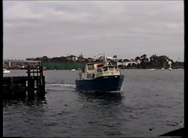 Vintage home movie footage captures a small blue and white ferry departing from a wooden pier on a cloudy day