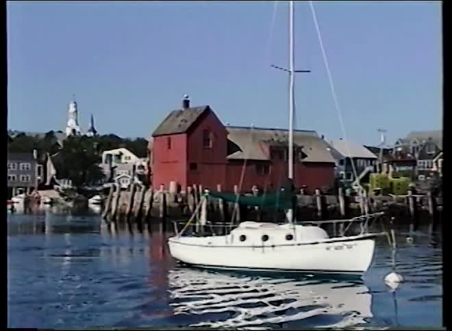 A classic sailboat bobs peacefully in the harbor in front of Rockport's iconic red fishing shack, Motif Number 1, on a clear day