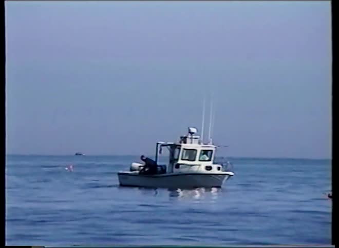 A fisherman works from a small boat floating on the calm open ocean
