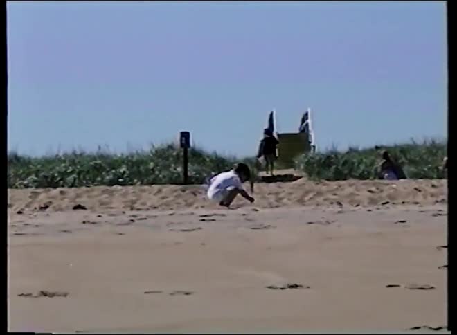 Vintage VHS footage captures a serene day at the beach where children play in the sand while adults relax