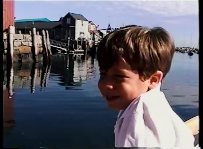 A young boy smiles while on a boat tour of a picturesque New England fishing harbor in this nostalgic vintage home video