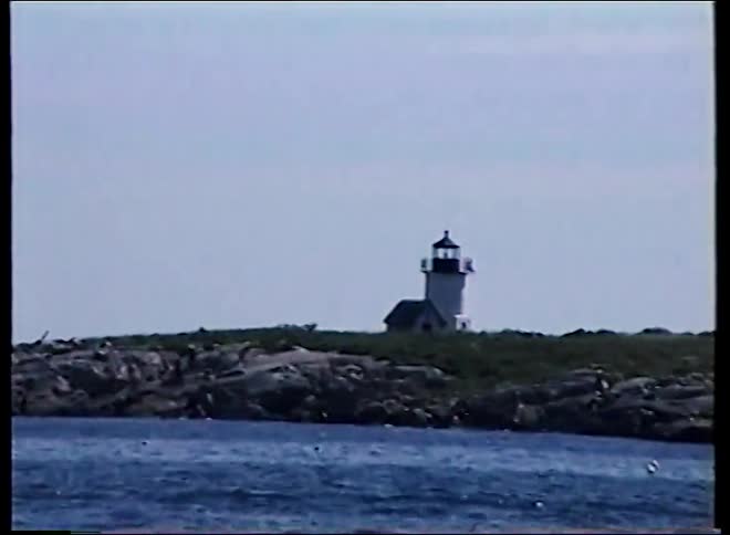 Archival footage shows a classic white lighthouse on a rocky island, seen from the choppy blue ocean