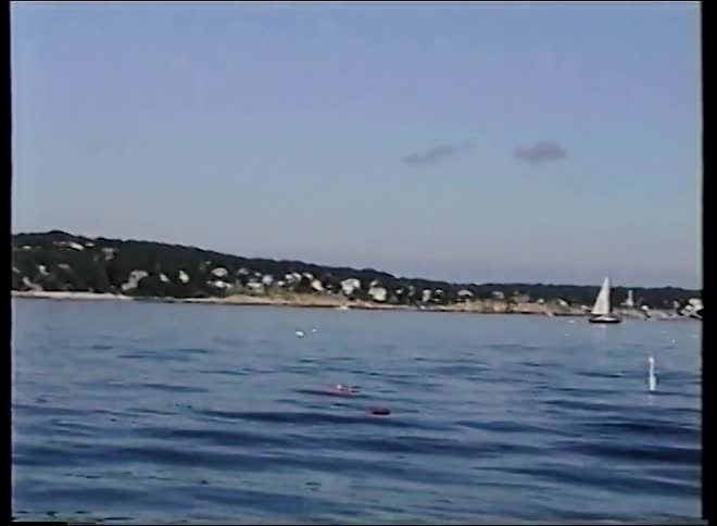 Vintage footage from a boat leaving a coastal town harbor and panning across the calm ocean waters