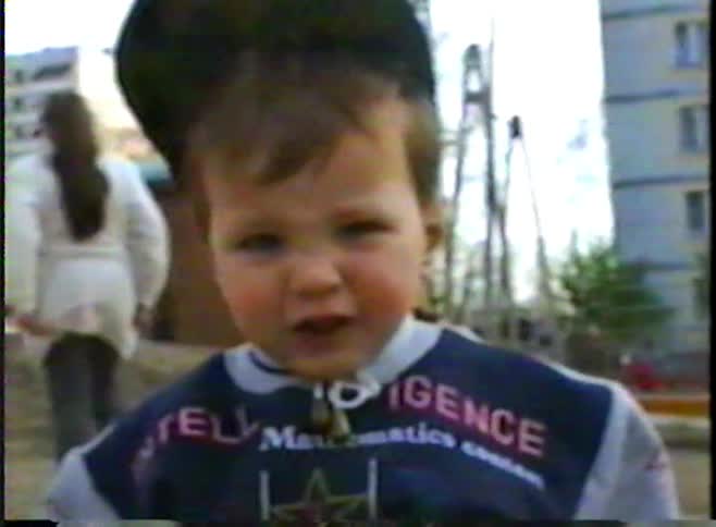 A vintage VHS home video captures a close-up of a young boy in a backwards cap at an urban playground