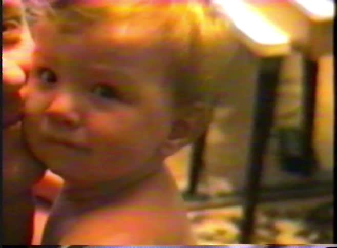 A father holds his sleepy, fussy baby boy in an endearing home video from the 1980s