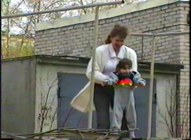 Vintage 90s home video of a mother helping her toddler play and hang from a backyard pull-up bar