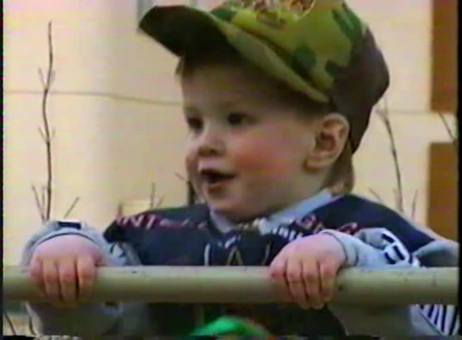 Vintage VHS footage shows a cute toddler in a camouflage cap happily climbing on a jungle gym at an urban playground