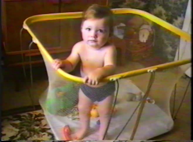 A happy baby boy laughs and smiles while standing in a playpen in a vintage-style home video