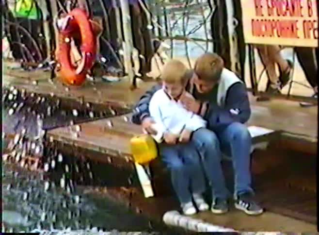 A beluga whale playfully splashes two young boys on a dock while a crowd watches in this vintage home video
