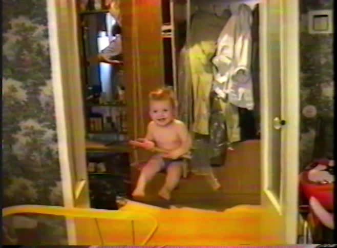 Cute baby in a diaper happily bounces and swings in a wooden indoor doorway jumper