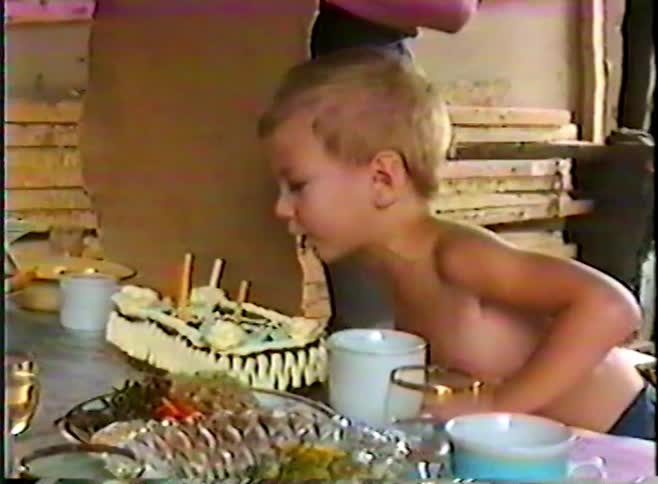 Young boy blows out birthday candles at a family table during a casual home celebration