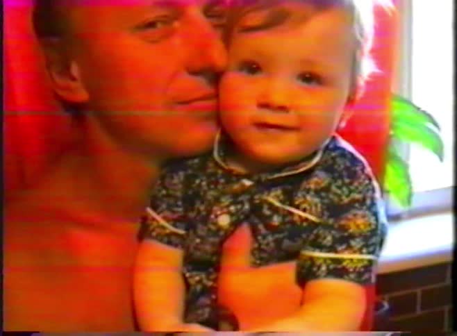 A loving grandfather smiles and holds his adorable baby grandchild in a warm, distorted home video from the 1990s